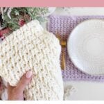 A hand holds a textured white crochet placemat above a table set with a white plate, gold cutlery, and a lavender crochet placemat, showcasing the beautiful results of a detailed crochet placemat pattern.