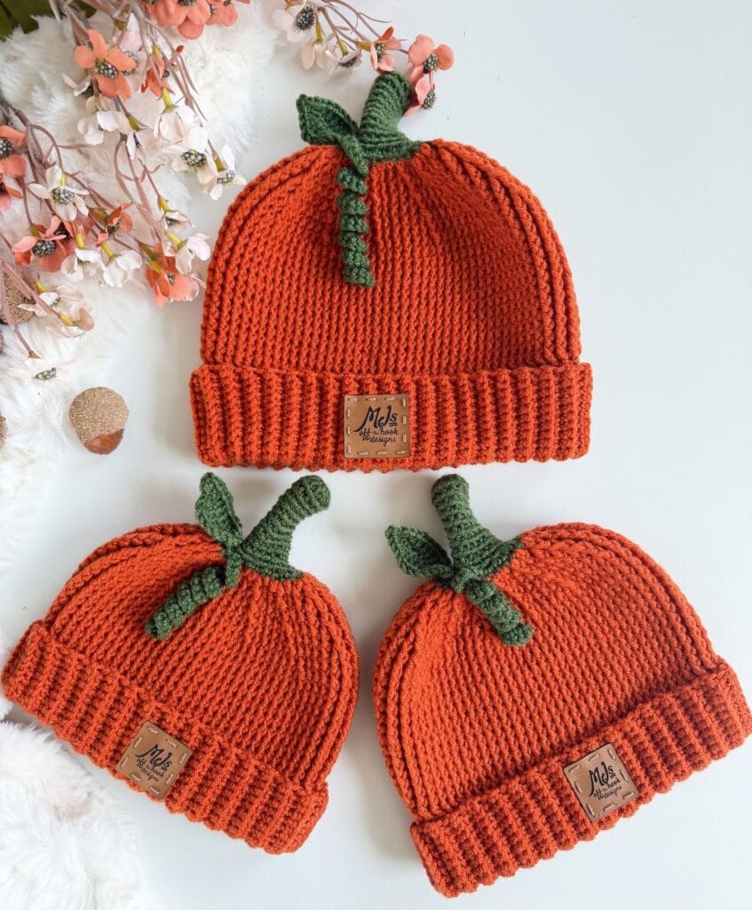 Three orange crochet pumpkin hat patterns with green stems and branded leather tags.