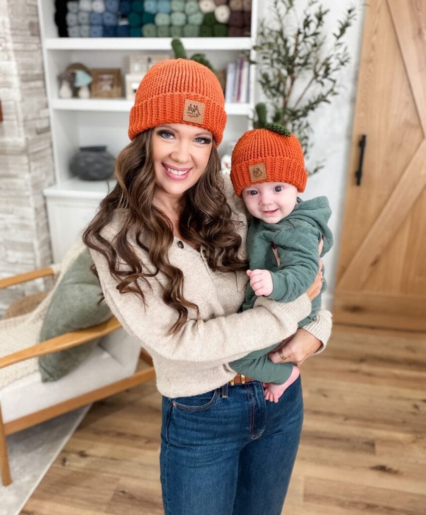A woman holding a baby, both wearing matching orange pumpkin hats crocheted from a pattern.